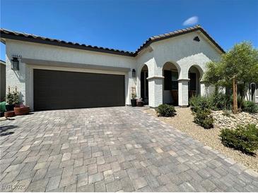 Inviting home featuring a two-car garage, paver driveway, arched entrance, and desert landscaping at 10064 Ocher Valley Ave, Las Vegas, NV 89178