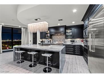 Modern kitchen boasts an island with seating, dark cabinetry, and a stunning chandelier overlooking city views at 9101 Alta Dr # 1206, Las Vegas, NV 89145