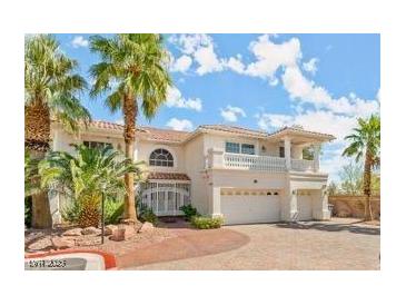 Elegant two-story home with a balcony, arched windows and mature palm trees at 7682 Calm Passage Ct, Las Vegas, NV 89139