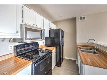 Compact kitchen features white cabinetry, wood countertops, and black appliances at 1381 E University Ave # 204, Las Vegas, NV 89119