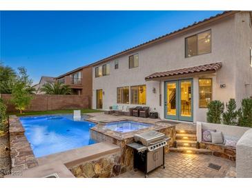 Beautiful backyard with pool, spa, outdoor kitchen, seating, and a two-story house with stucco exterior at 9950 Waxberry Ct, Las Vegas, NV 89178