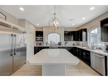 A spacious kitchen featuring black cabinets, stainless steel appliances, and a large center island with white countertops at 9835 Fox Estate St, Las Vegas, NV 89141