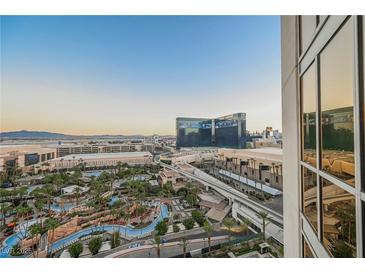Expansive view features a resort pool, palm trees, the Las Vegas Strip, and a clear blue sky at 145 E Harmon Ave # 1202, Las Vegas, NV 89109