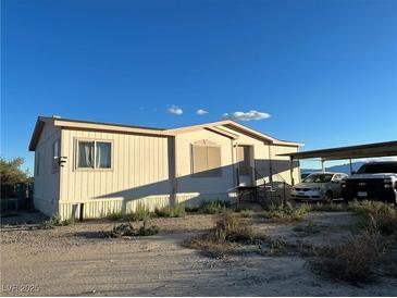 View of the house featuring a quaint exterior, access stairs, desert landscape, and a covered parking area at 2471 Mcmurray Dr, Pahrump, NV 89060