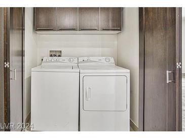 A clean and well-organized laundry area with a white washer and dryer, and upper cabinets for storage at 8925 W Flamingo Rd # 110, Las Vegas, NV 89147