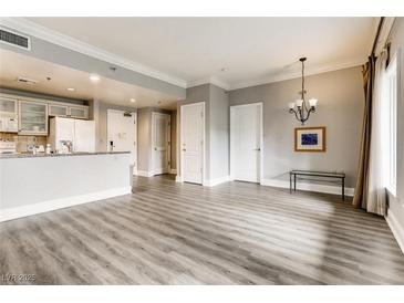 Open-concept living room with light gray walls, hardwood flooring, chandelier, and a partial kitchen view at 30 Strada Di Villaggio # 143, Henderson, NV 89011