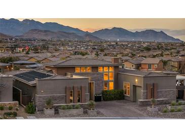 Stunning exterior view of a modern home with beautiful stonework, landscaping, and a mountain backdrop at sunset at 10096 Amethyst Hills St, Las Vegas, NV 89148