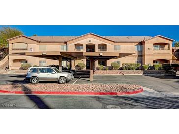 Tan apartment building with covered parking, landscaping, and parking spots at 5751 E Hacienda Ave # 172, Las Vegas, NV 89122