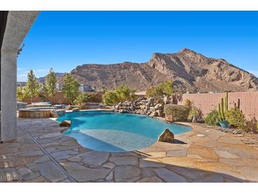 Backyard pool area with desert landscaping, stone waterfall feature, integrated hot tub, and mountain views at 4081 Turquoise Falls St, Las Vegas, NV 89129