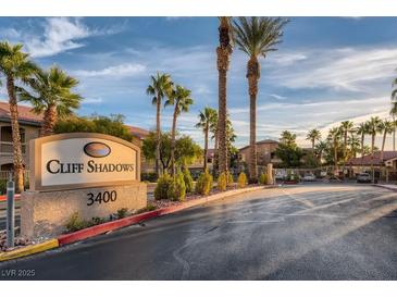 View of the Cliff Shadows community entrance featuring a stone sign, palm trees, and well-maintained landscaping at 3451 Desert Cliff St # 103, Las Vegas, NV 89129