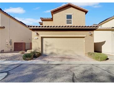 Tan home featuring a two-car garage with a brick paver driveway and well-maintained desert landscaping at 7059 Mackenzie Bay Ave, Las Vegas, NV 89179