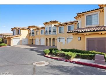 A sunny view of a multi-unit stucco home with garages, tidy landscaping, and ample parking at 21 Via Visione # 201, Henderson, NV 89011