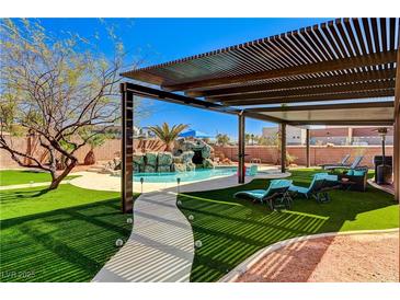 Inviting backyard oasis with a sparkling pool, rock waterfall, pergola, and comfortable lounge seating on lush artificial turf at 6689 Sparks Ave, Las Vegas, NV 89142