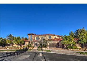 Elegant two-story home featuring a stone facade, arched windows, tile roof, and lush landscaping at 6 Fire Rock Ct, Las Vegas, NV 89141