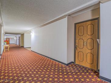 View of the carpeted hallway leading to unit, with a wooden door to the right at 725 N Royal Crest Cir # 213, Las Vegas, NV 89169