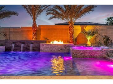 Stunning pool with water features, spa, and fire pit, surrounded by lush landscaping and ambient lighting at 9091 Becket Ranch Ct, Las Vegas, NV 89113