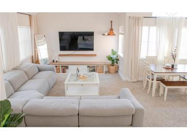 Bright living room with a large sectional sofa, modern TV, and a dining area near the window at 425 Donner Pass Dr, Henderson, NV 89014