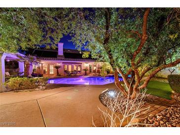 A stunning backyard at night showcasing a sparkling pool, mature trees, and an inviting outdoor living space at 692 Quilt Pl, Henderson, NV 89052