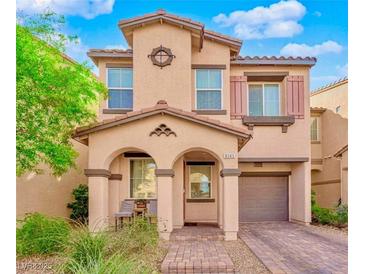 Charming two-story home with a covered entry, arched columns, tan stucco, and a lush landscaped yard and brick paver driveway at 8349 Spruce Bay Ave, Las Vegas, NV 89178