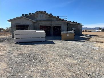 Unfinished home featuring a three-car garage with a gravel yard and mountain views in the background at 1831 E Deerskin St, Pahrump, NV 89048