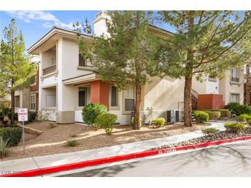 Condo exterior featuring neutral stucco, desert landscaping, trees, and private balcony at 913 Duckhorn Ct # 204, Las Vegas, NV 89144