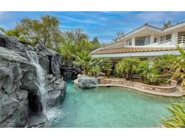 Beautiful backyard pool featuring a rock waterfall and lush tropical landscaping at 2221 S Tioga Way, Las Vegas, NV 89117