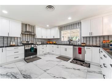 Modern kitchen with white cabinets, stainless steel appliances, black countertops, and stylish backsplash at 1920 Parkchester Dr, Las Vegas, NV 89108