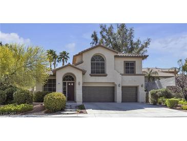 Two-story home featuring a front yard with mature landscaping, a two car garage and classic desert architecture at 3047 Whispering Crest Dr, Henderson, NV 89052