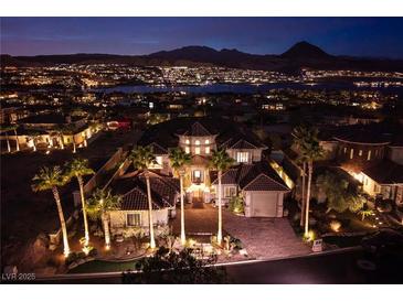 Stunning home exterior with lush landscaping, a circular driveway, and a view of the city lights at 10 Via Potenza Ct, Henderson, NV 89011