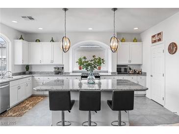 Bright kitchen with granite counters, white cabinets, stainless appliances, a large island with seating, and pendant lighting at 6346 Rock Strm Ln, Las Vegas, NV 89141