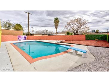 Backyard pool with diving board is surrounded by concrete and enclosed by red brick wall at 3008 Lawndale St, Las Vegas, NV 89121
