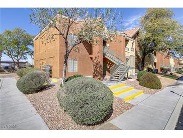 Exterior view of condo building featuring stucco walls, stairs, and manicured landscaping with trees and shrubs at 2120 Ramrod Ave # 1318, Henderson, NV 89014