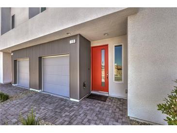 Modern home featuring a gray exterior, two-car garage, brick paver driveway, and a vibrant orange front door at 8629 Ensworth St # 113, Las Vegas, NV 89123