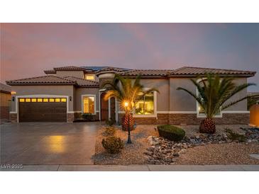 Inviting home exterior with a two-car garage, desert landscaping, and warm exterior lighting at 7682 Rafter Ct, Las Vegas, NV 89139
