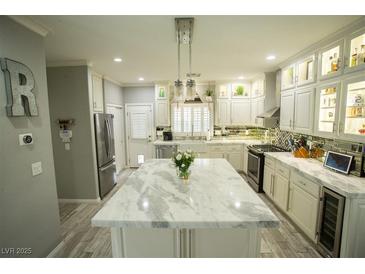 Bright kitchen with white cabinets, large island, stainless steel appliances and gray wood-look tile floors at 10323 Hardy Falls St, Las Vegas, NV 89141