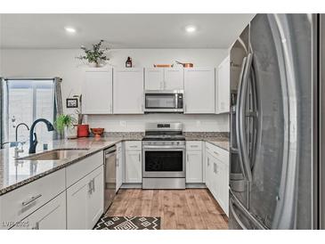 Modern kitchen featuring stainless steel appliances and granite countertops, wooden floors and white cabinetry at 7456 Cooks Meadow St, North Las Vegas, NV 89084