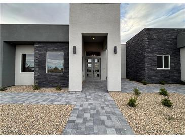Modern home featuring a stone facade, sleek gray accents, and a paved walkway leading to the glass-paneled front door at 5719 Christian Creek Ct, Las Vegas, NV 89149