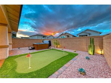 Inviting backyard featuring a putting green, hot tub, desert landscaping, and beautiful sunset at 122 Cabaletta Ln, Henderson, NV 89015