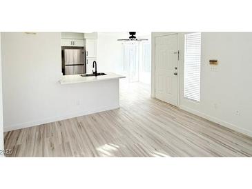 Bright living room features white walls, wood-look floors, and access to the kitchen and front door at 5222 Mandalay Springs Dr # 202, Las Vegas, NV 89120