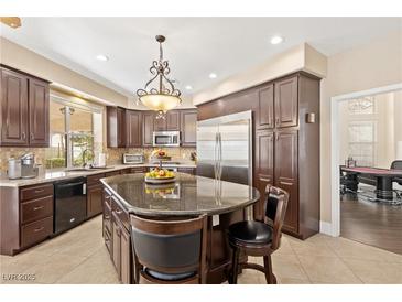 Bright kitchen features a granite island, stainless steel refrigerator, dark wood cabinets, and elegant chandelier at 9517 Spanish Steps Ln, Las Vegas, NV 89117