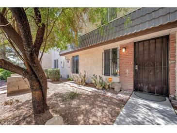 Charming condo exterior with a secure iron door and desert landscaping and mature shade tree at 3944 Visby Ln, Las Vegas, NV 89119