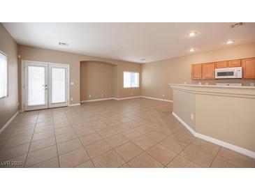 Spacious living room with tile flooring and natural light from the double french doors and the adjacent kitchen area at 10643 Petricola St # 103, Las Vegas, NV 89183
