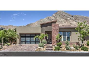 Modern home featuring beautiful desert landscaping, a glass garage door and striking mountain views at 11185 Black Fire Opal Dr, Las Vegas, NV 89138