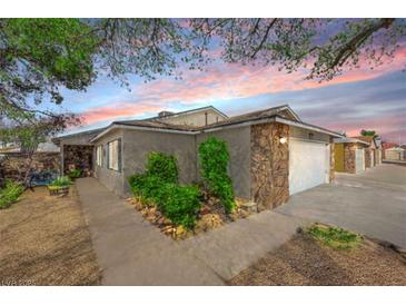 Single-story home with a stone accent wall, attached garage, concrete driveway, and desert landscaping beneath a colorful sunset sky at 4655 Fire Fly Cir, Las Vegas, NV 89122