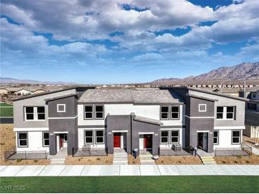 Modern townhomes showcase sleek, two-tone exteriors with private entrances, nestled against a backdrop of mountains and blue skies at , North Las Vegas, NV 89084