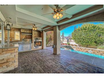 An outdoor kitchen with stone accents, a fireplace, and a view of the refreshing pool area at 7420 Enchanted Hills Ct, Las Vegas, NV 89129