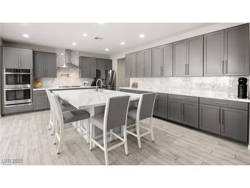 Bright kitchen features gray cabinetry, stainless appliances, tile backsplash, and a large center island with bar seating at 70 Pikiariki Ct, Las Vegas, NV 89183