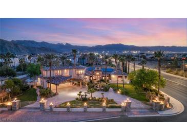 Stunning exterior view of grand estate with palm trees, lush landscaping, and mountain backdrop at sunset at 4775 N Tee Pee Ln, Las Vegas, NV 89129