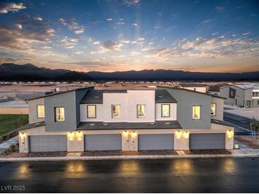 Modern townhome exterior featuring attached garages, neutral tones, and mountain views at sunset at 6157 Aster Garden St # 153, North Las Vegas, NV 89081