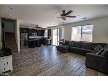 Open-concept living room features wood tile floors, ceiling fan, and gray sofa with a kitchen view at 386 Espressivo St, Henderson, NV 89011